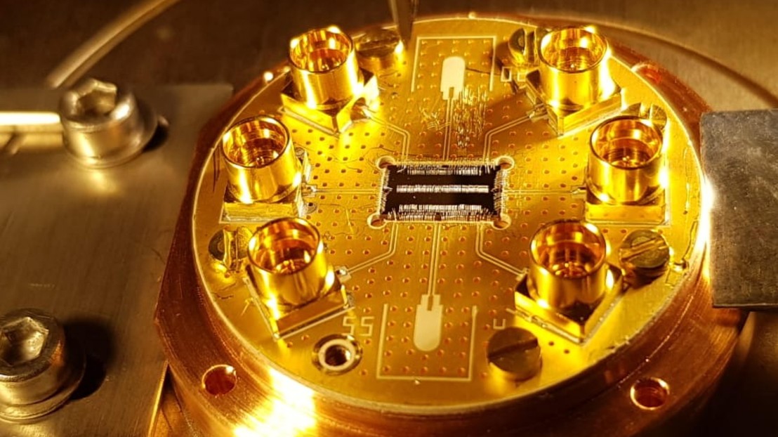 Chip with the couple cavity arrays (CCAs) wire bonded to a printed circuit board on top of a copper holder. 2025 EPFL/HQC - CC-BY-SA 4.0 Chip with the couple cavity arrays (CCAs) wire bonded to a printed circuit board on top of a copper holder. 2025 EPFL/HQC - CC-BY-SA 4.0